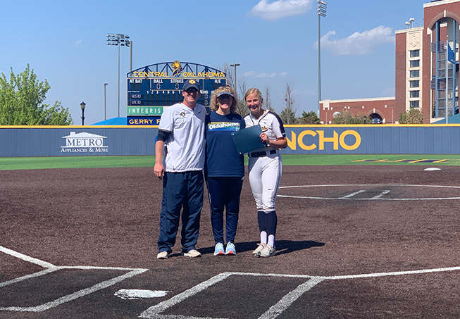 Softball Coach Cody White, Dr. Gerry Pinkson and pitcher Kylee Lynch stand on softball field