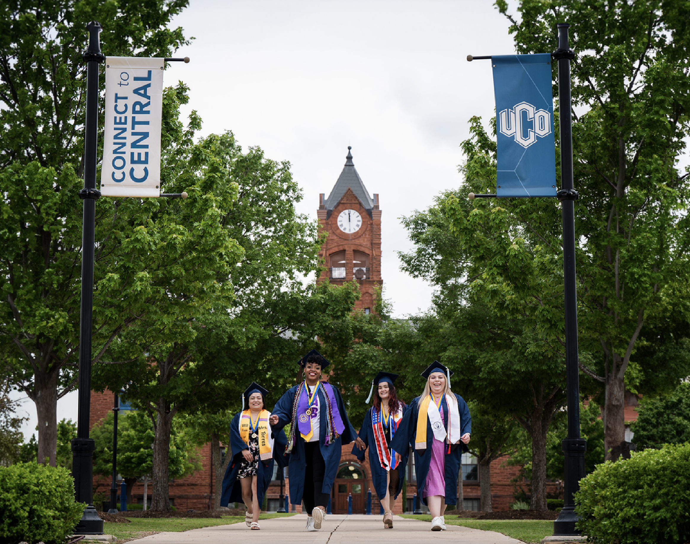 Image of four UCO graduates walking in front of Old North on campus