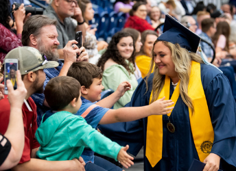 Photo of graduate greeting family who is sitting in the stands during Graduation
