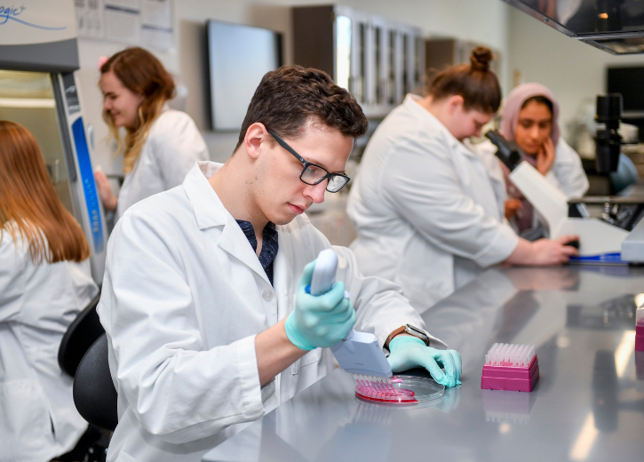 A UCO student in a lab coat works in a lab.