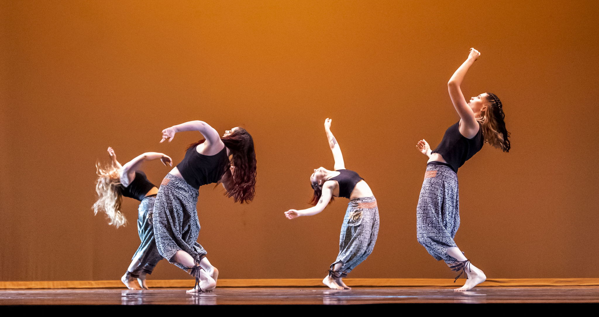 Four UCO Kaleidoscope Dance Company members performing on stage.