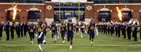 Photo of the UCO Football Team running onto the field at Wantland Stadium
